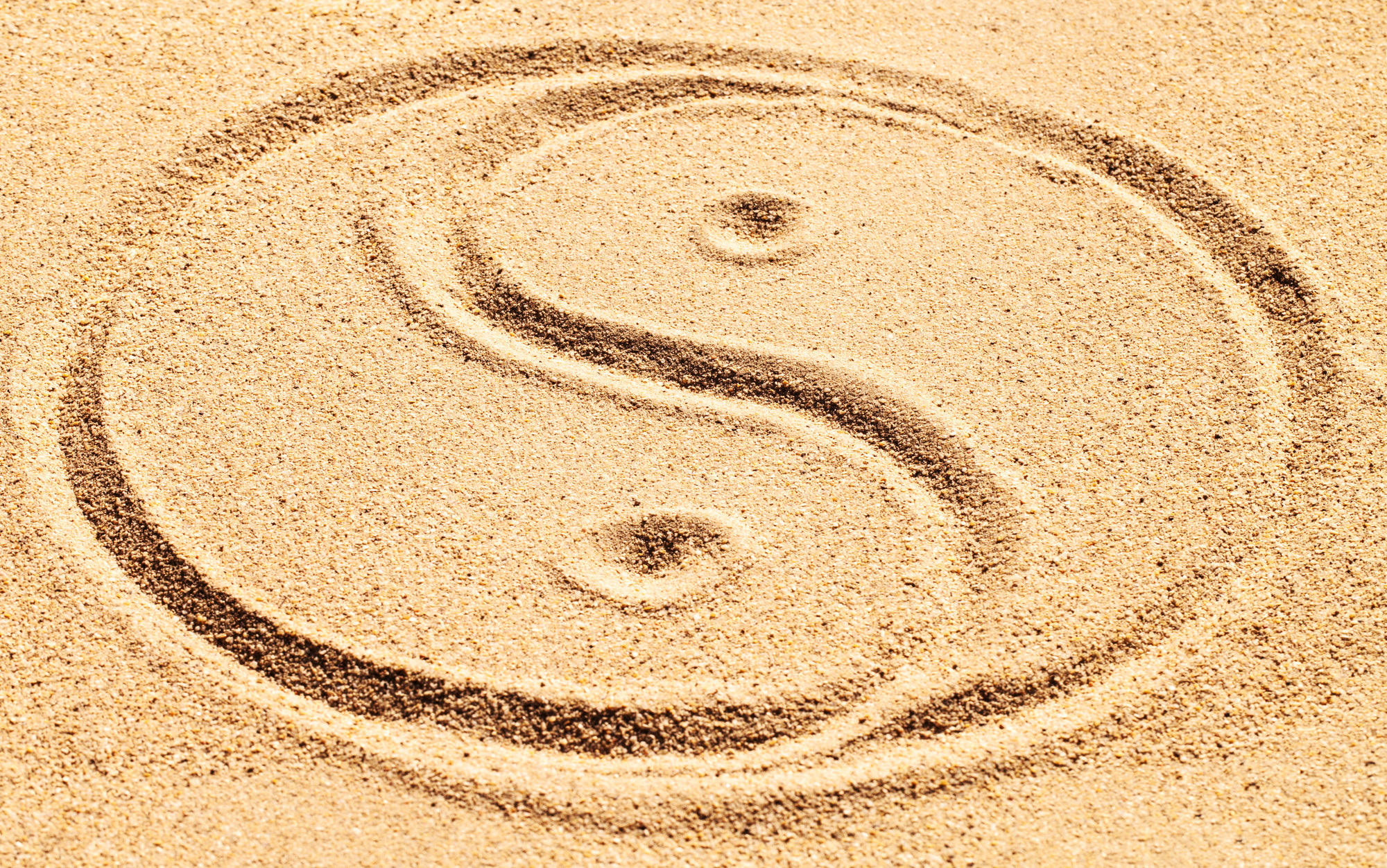 Balance is achievable. Shot of a yin and yang symbol drawn in sand.