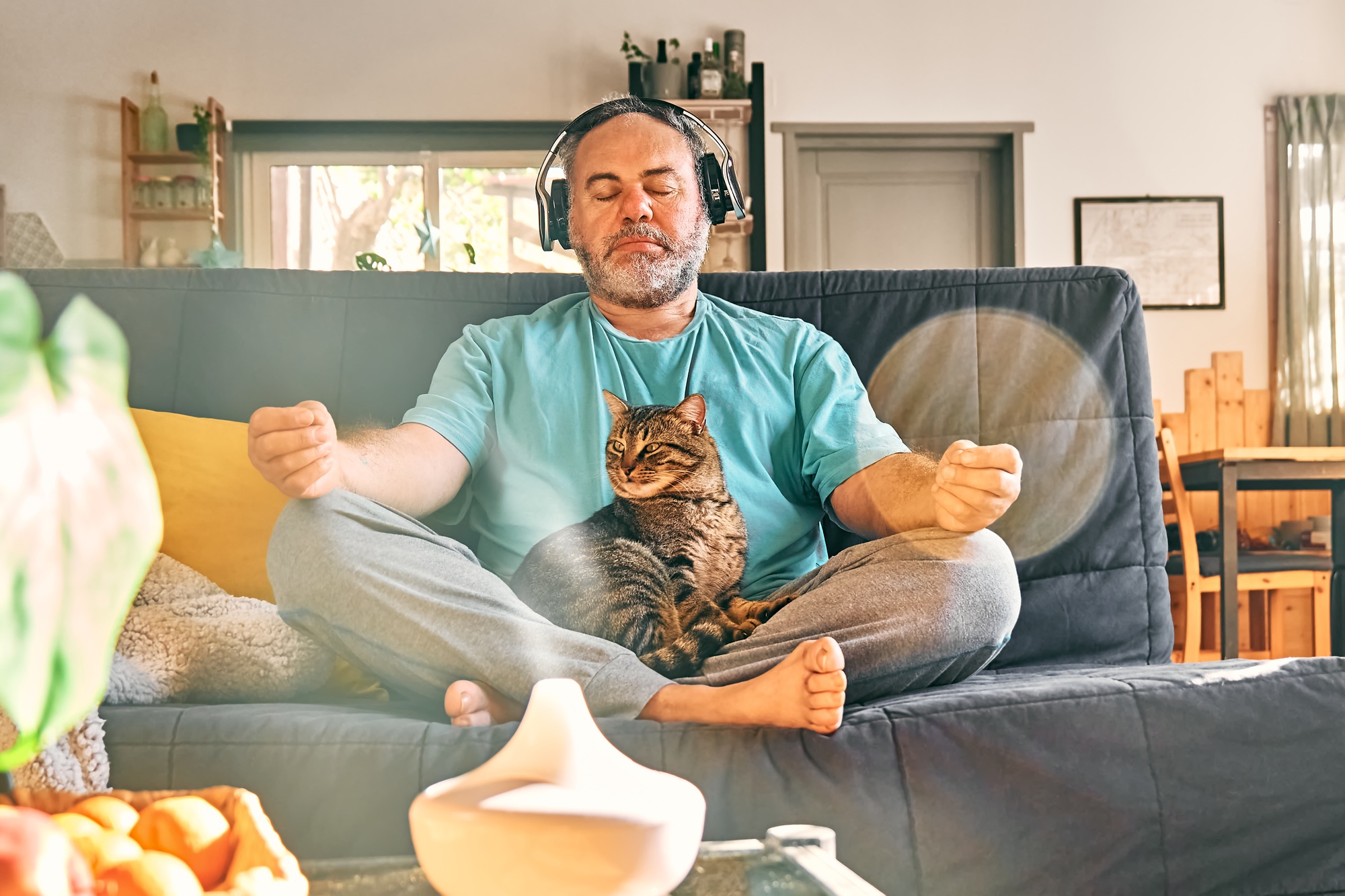 Mature middle-aged overweight man in wireless headphones meditation at home with his cat.