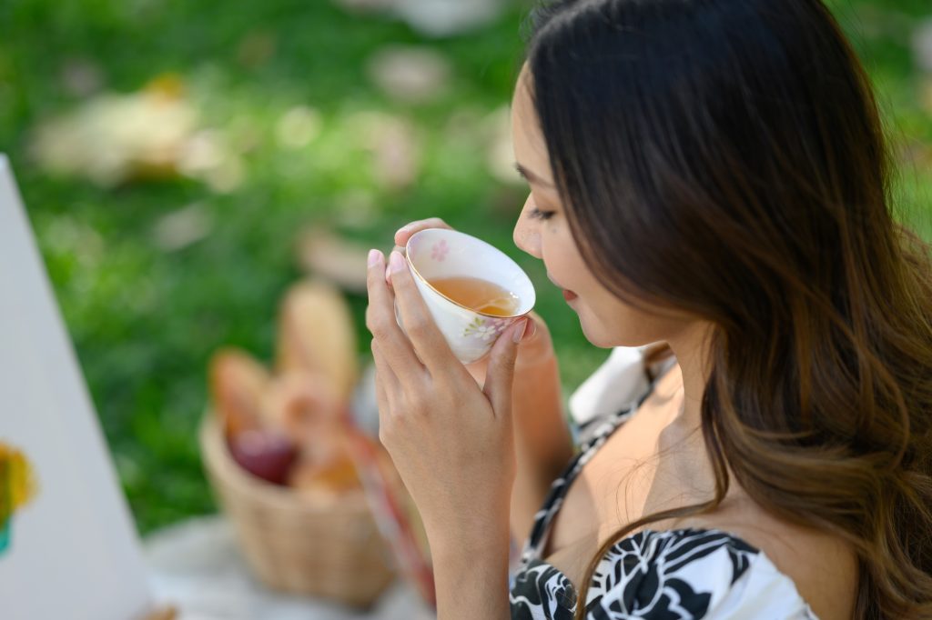 Millennial woman enjoying a cup of tea while relaxing in garden. Self care and mental health concept